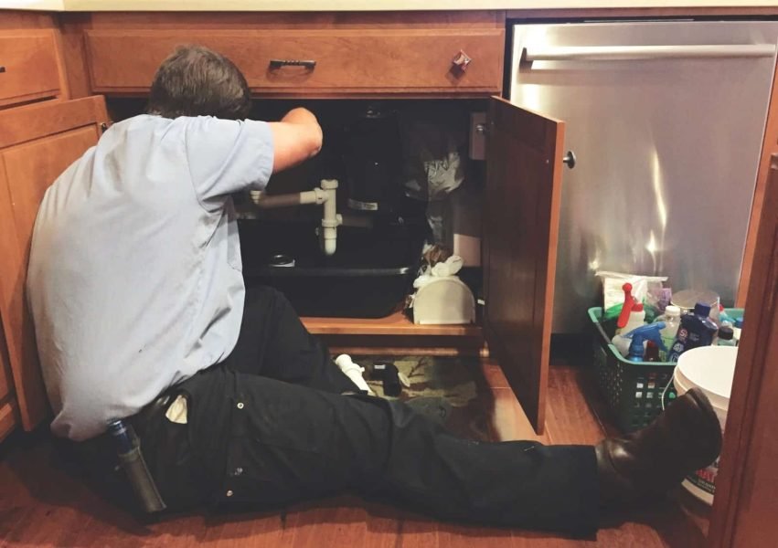 Plumber fixing kitchen sink pipes to prevent leaks and water damage.