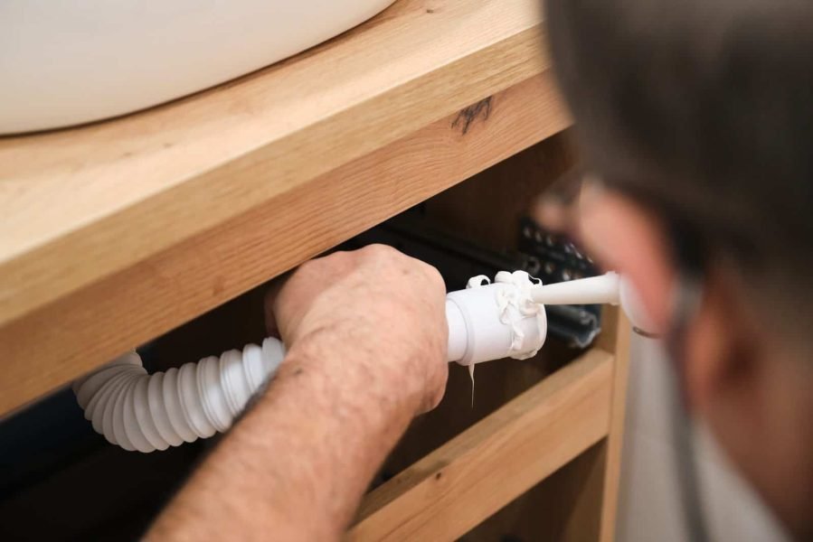 Emergency plumbing repair under kitchen sink with pipe inspection.